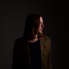 a man with long hair wearing a leopard print blazer and black t - shirt