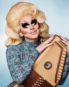 a woman with long blonde hair and black eyeliners holding a musical instrument in her hands