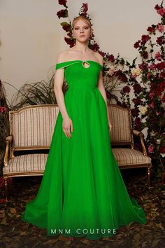 a woman in a long green dress standing next to a couch with flowers on it