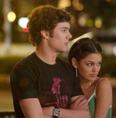 a young man and woman standing next to each other in front of a street at night