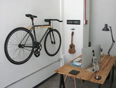 a bicycle mounted to the wall next to a desk with a computer and laptop on it