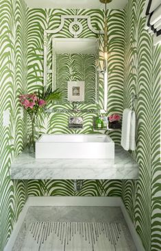 a bathroom with green and white wallpaper, marble counter top, sink and mirror