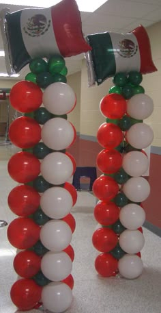 two red, white and green balloons are attached to poles in the middle of a hallway