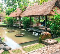 a man sitting on a bench in front of a small pond with rocks and plants