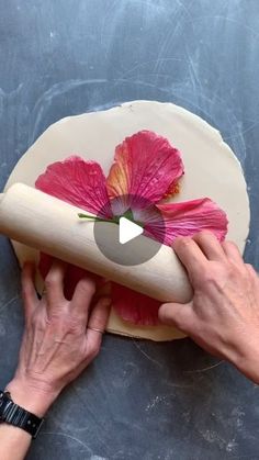 a person rolling out a flower on top of a doughnut with a rolling pin