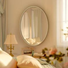 a round mirror on the wall above a bed in a room with white walls and pillows