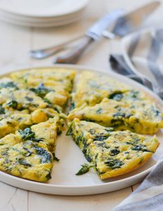 an omelet with spinach and cheese on a white plate next to silverware