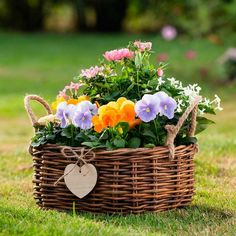 a basket filled with flowers sitting on top of a lush green field next to a heart shaped tag