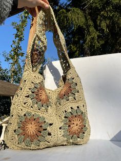 a hand holding a crocheted purse on top of a white surface with trees in the background