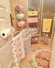 a bathroom with pink and yellow towels hanging on the shower curtain, toilet paper roll holder, and towel rack