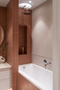 a bath tub sitting next to a white sink under a round mirror in a bathroom