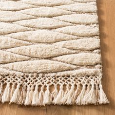 a white rug with tassels on top of a wooden floor next to a wood floor