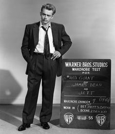 a man in a suit and tie standing next to a sign with writing on it