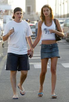 a young man and woman walking down the street holding hands, both looking at each other