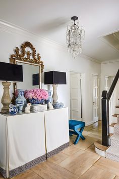 a living room filled with furniture and a chandelier above a white table topped with flowers