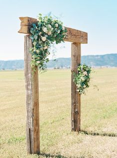 a wooden arch decorated with flowers and greenery for an outdoor ceremony in the middle of a field