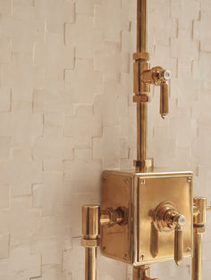 a gold square shaped shower faucet in front of a white brick wall