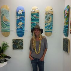 a woman wearing a hat standing in front of surfboards hanging on the wall behind her