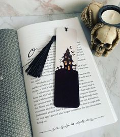 a bookmark with a house on it sitting on top of an open book next to a candle