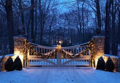 a white gate with christmas lights on it in the middle of a snow covered driveway