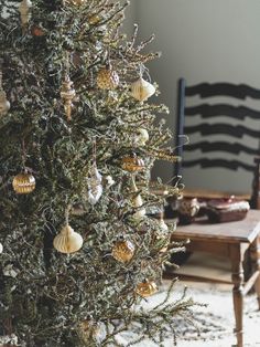 a christmas tree with ornaments hanging from it's branches in front of a chair