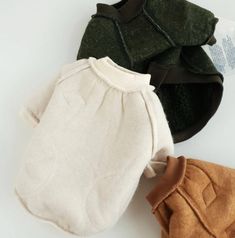 three baby sweaters are laying next to each other on a white surface, one is green and the other is brown