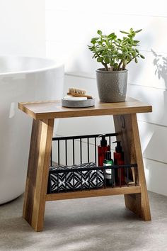 a small wooden table with a plant on it next to a bathtub and toilet