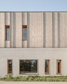 the side of a building with three windows and grass growing on the ground in front of it