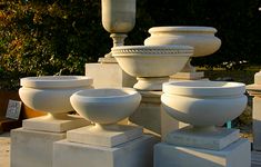 many white vases are stacked on top of each other in front of some bushes