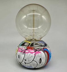 a glass ball sitting on top of a table next to a light bulb with cartoon characters painted on it