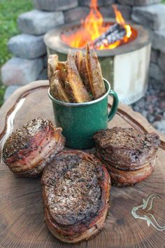 steaks and french fries are sitting on a table next to an open fire pit