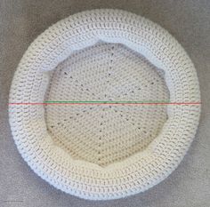 a white crocheted object with red and green lines in the center on a gray surface