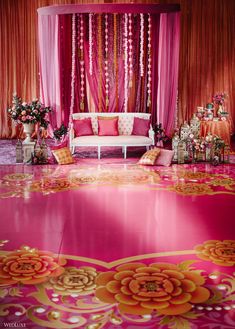 a pink and gold decorated stage with flowers on the floor, couches and curtains