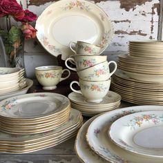 a table topped with lots of white and gold plates covered in floral designs next to a vase filled with red flowers