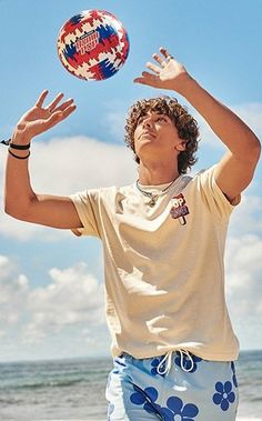 a young man is playing with a ball on the beach in front of the ocean