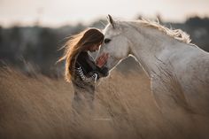 a woman standing next to a white horse on top of a dry grass covered field