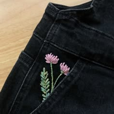 a pair of black jeans with pink flowers embroidered on the front and back pocket, sitting on a wooden surface