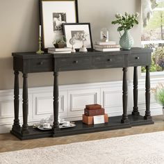 a black table with two drawers and pictures on it next to a plant in a vase