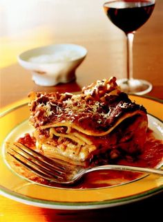 a plate with lasagna on it next to a glass of wine and a fork