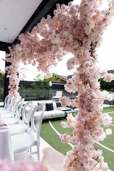 the table is set with white chairs and pink flowers hanging from the ceiling, along with an artificial grass field