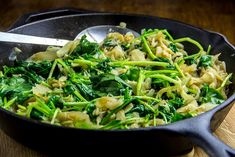 a skillet filled with green vegetables on top of a wooden table