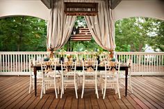 an outdoor dining area with white chairs and table set up for a formal dinner on the deck