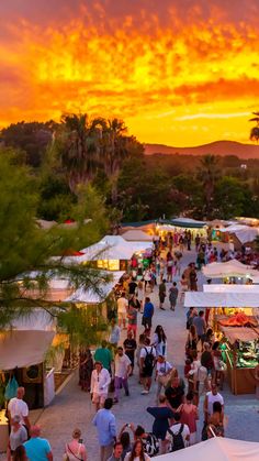 a crowd of people walking down a street next to tents and trees under a colorful sky