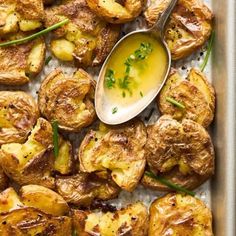 a pan filled with cooked potatoes and dipping sauce on top of the potatoes is garnished with chives