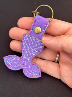 a hand holding a purple key chain with a mermaid tail on it's side