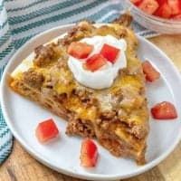 a piece of pie on a plate with strawberries and whipped cream in the background