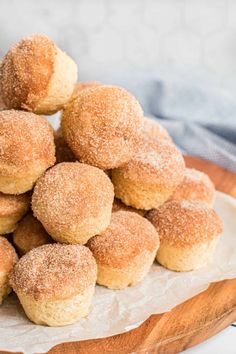 a pile of sugared doughnuts on a wooden platter with a napkin