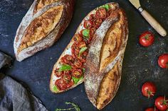 two loaves of bread with tomatoes on the side and a knife next to them