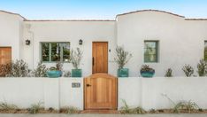 a white stucco house with wooden doors and plants on the outside wall in front of it