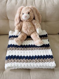 a stuffed animal sitting on top of a crocheted blanket in the shape of a bunny